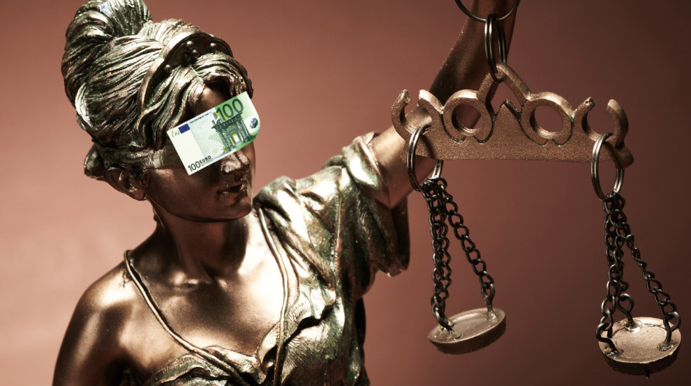 Justitia hält ihre Waage hoch, während ihr die Augen mit einem Geldschein verdeckt sind